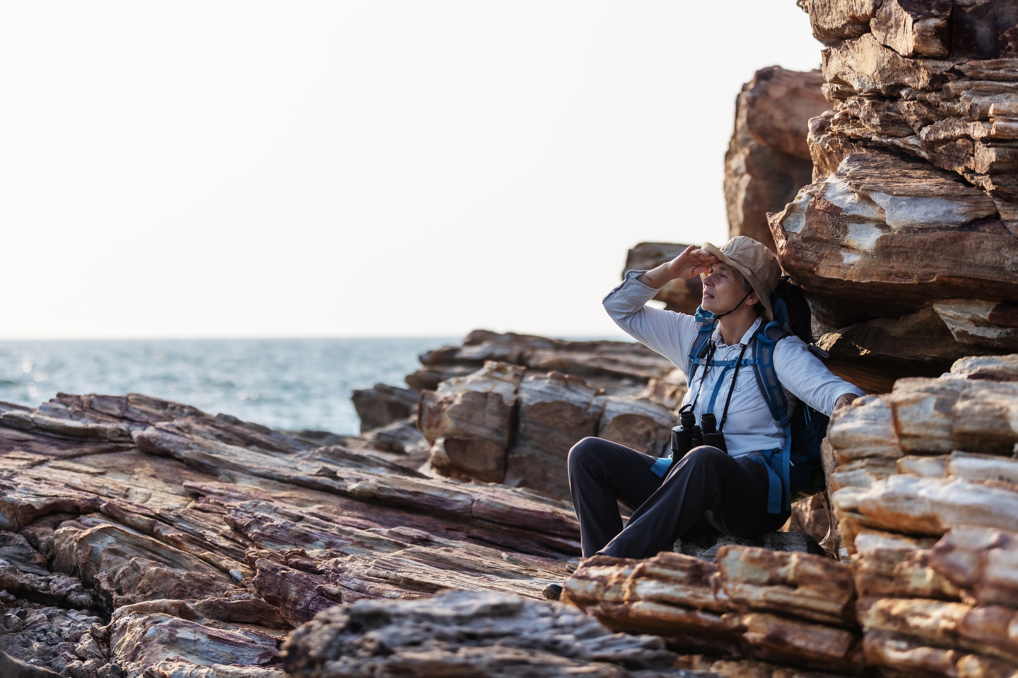 A senior explorer rests on rocky terrain by the sea