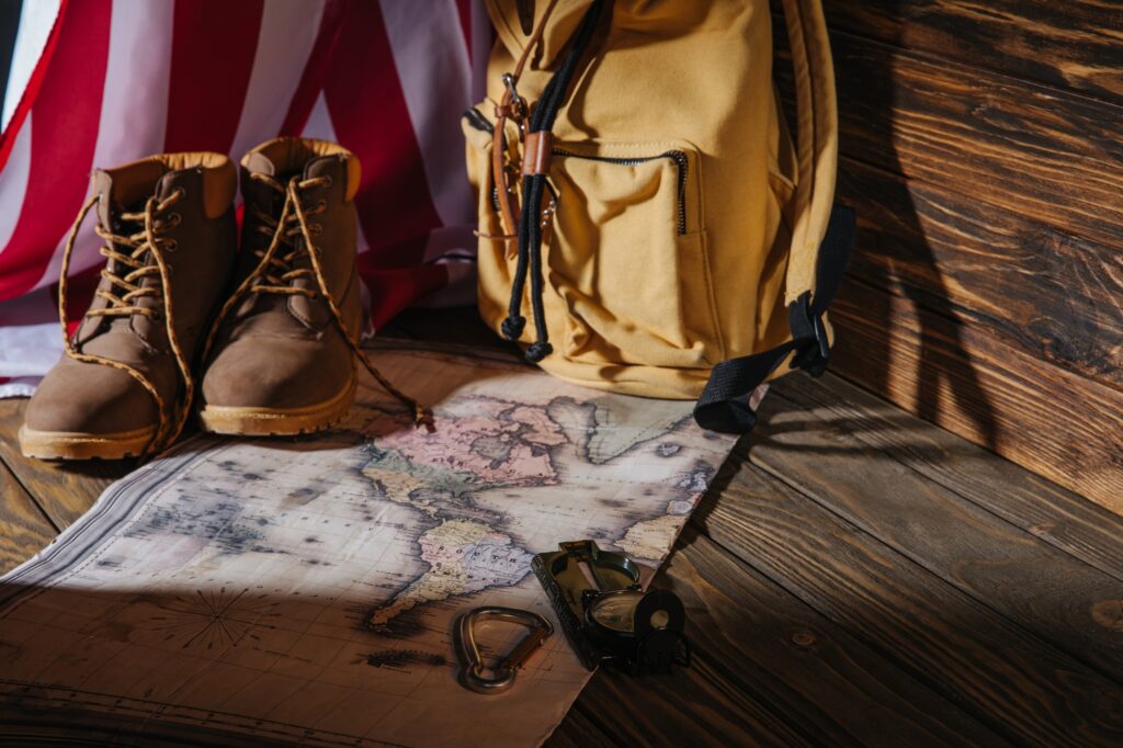 trekking boots, hiking equipment, map, backpack and american flag on wooden surface